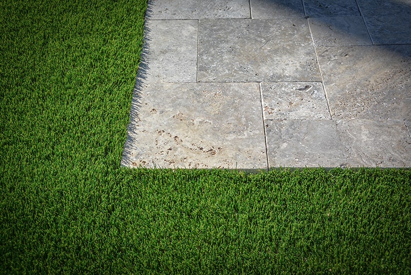 Artificial grass next to travertine stone pavers